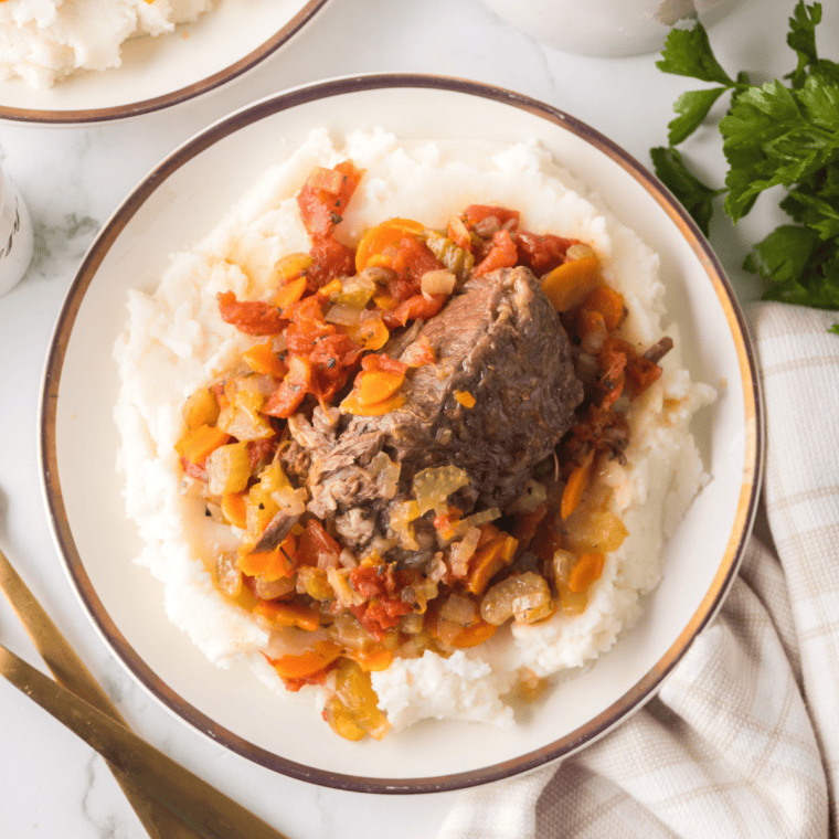 Close-up of Ninja Foodi Beef Osso Buco with braised beef shanks in a rich sauce, served over mashed potatoes.