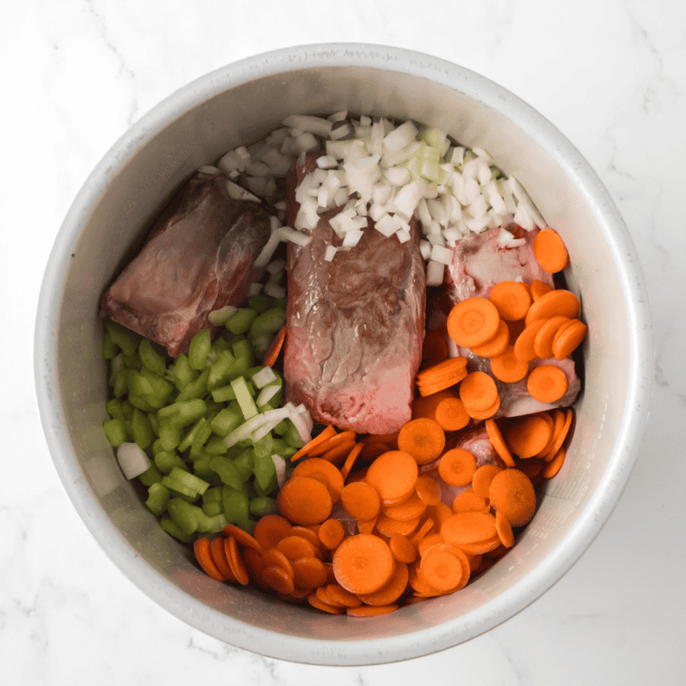 Beef searing in a Ninja Foodi on sauté mode with chopped celery, carrots, and onions being added to the pot.