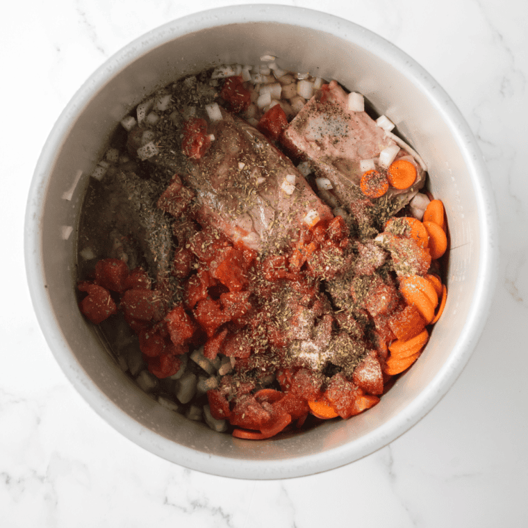 Ingredients including spices, white wine, beef broth, and diced tomatoes being stirred into a Ninja Foodi with beef and vegetables.