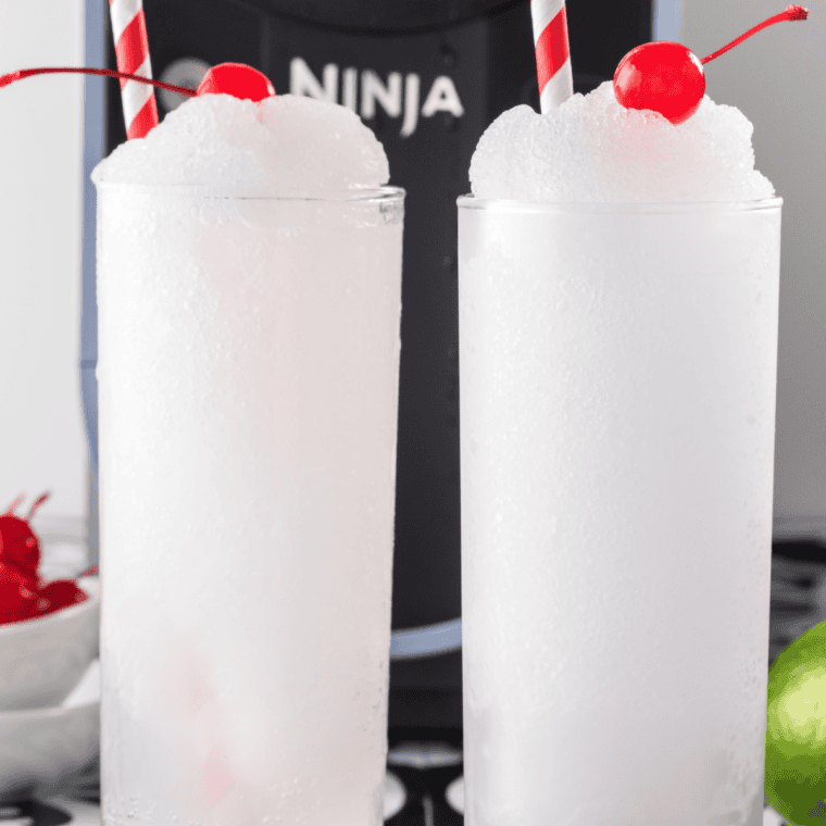 A vibrant red Ninja Slushi Cherry Slushie in a glass, topped with a straw and fresh cherries.