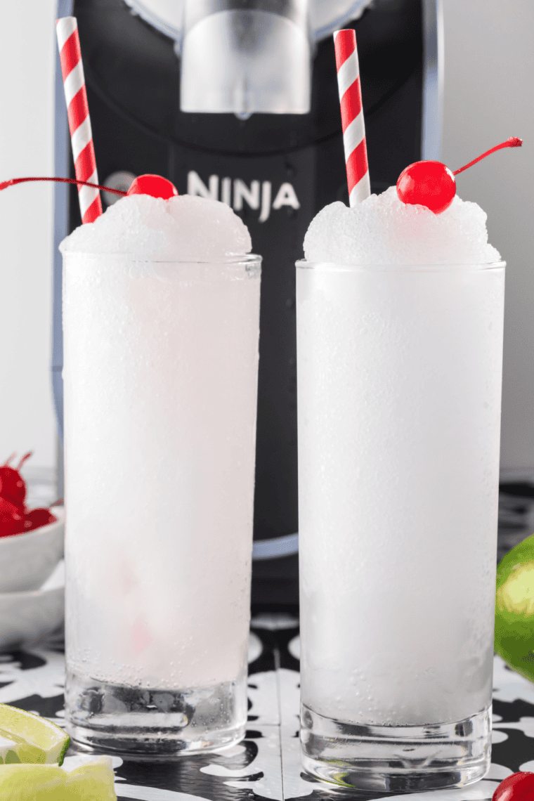 Colorful Ninja Slushi Cherry Slushi in a glass, topped with a straw and fresh cherries, ready to refresh you on a hot day.