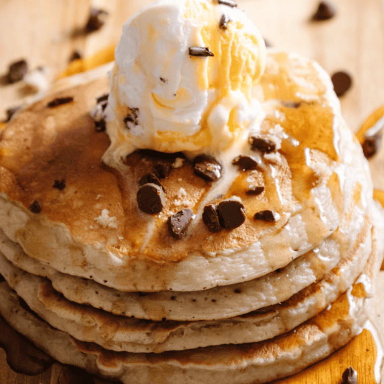 Stack of fluffy pancakes cooked on a Ninja Woodfire Grill, topped with syrup and fresh berries outdoors