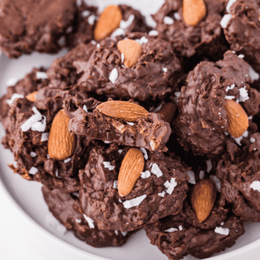 Close-up of Slow Cooker Almond Joy Chocolate Clusters made with melted chocolate, shredded coconut, and whole almonds, arranged on parchment paper.