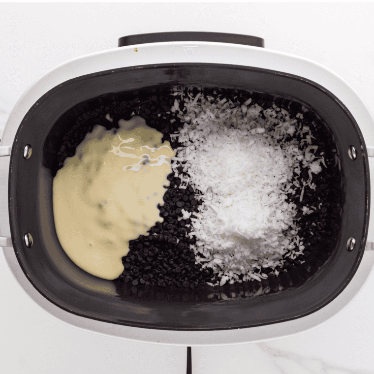 Ingredients including chocolate chips, coconut, and sweetened condensed milk being stirred together in a slow cooker.