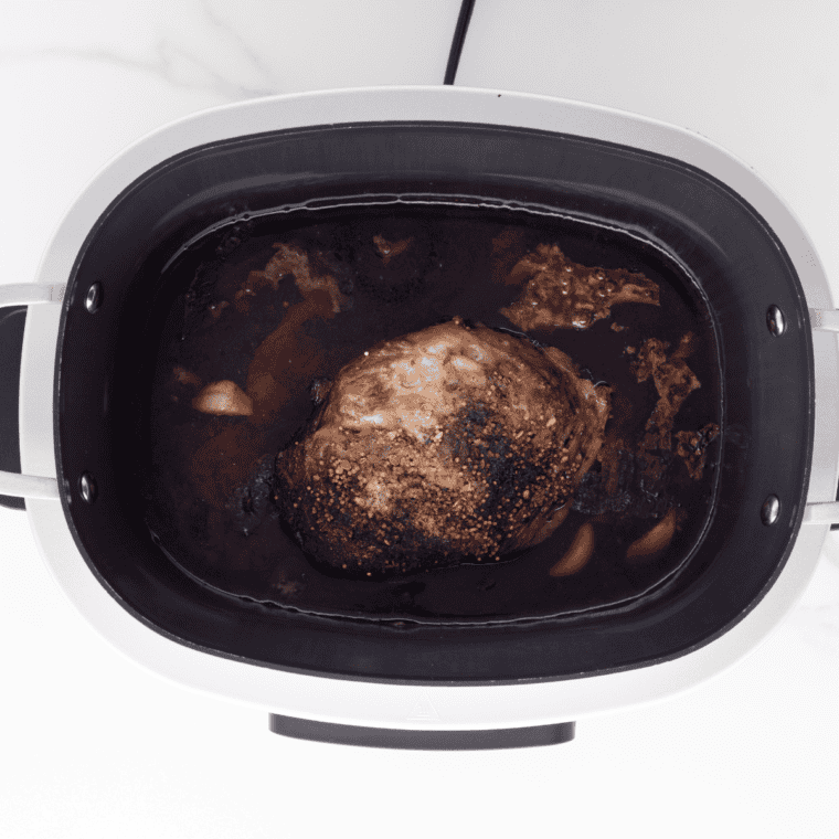 Seasoned beef brisket in the slow cooker before cooking, topped with pastrami spice rub