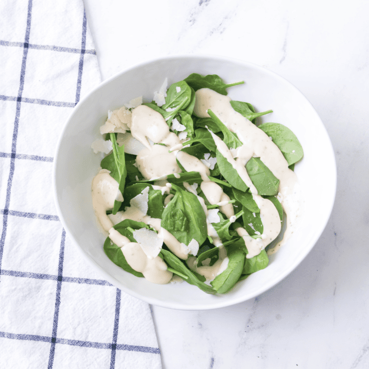 Chopped romaine lettuce in a large bowl being tossed with spicy Caesar dressing.
