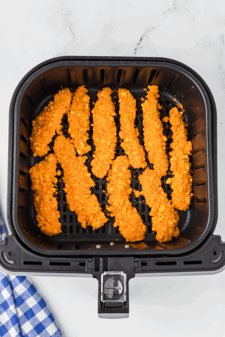 Cheetos-coated chicken strips arranged in a single layer in the air fryer basket