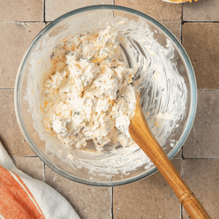 Mixing cream cheese, sour cream, cheddar, bacon, and seasonings in a bowl.