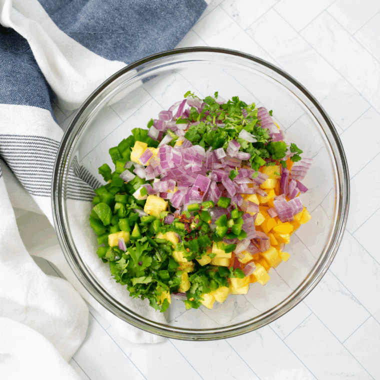 Diced mango, pineapple, papaya, red onion, and cilantro tossed in a bowl for tropical salsa