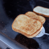 Crispy slices of golden toast cooking on a Blackstone griddle.