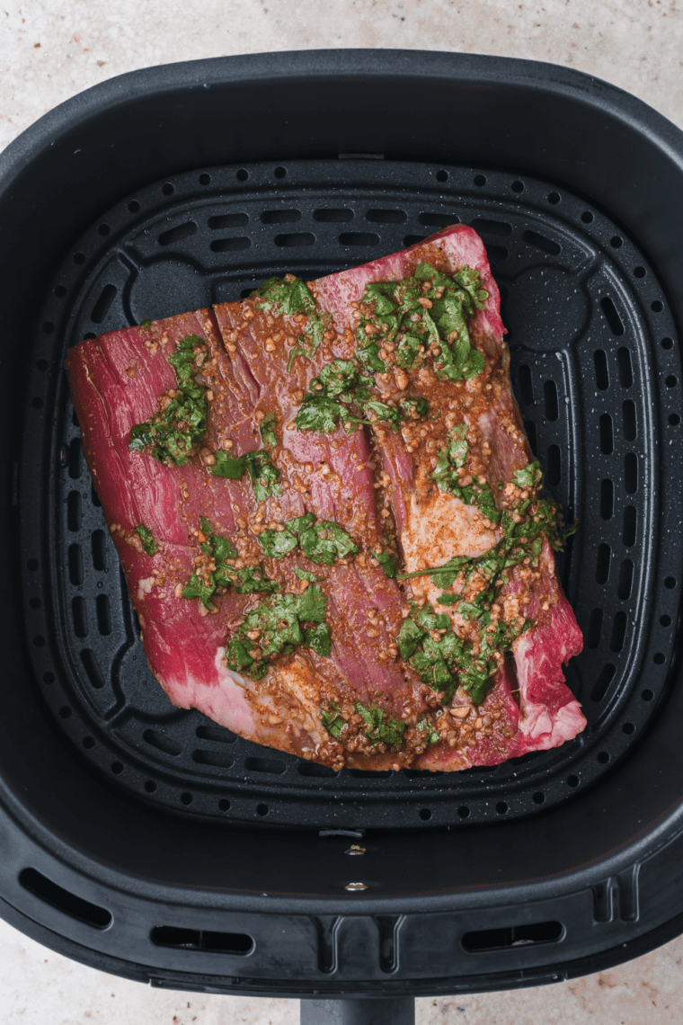 Air fryer carne asada steak cooking in basket after marinating, ready to slice for salad.