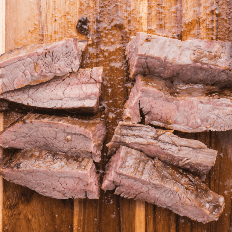 Cut up cooked carne asada on wooden cutting board.