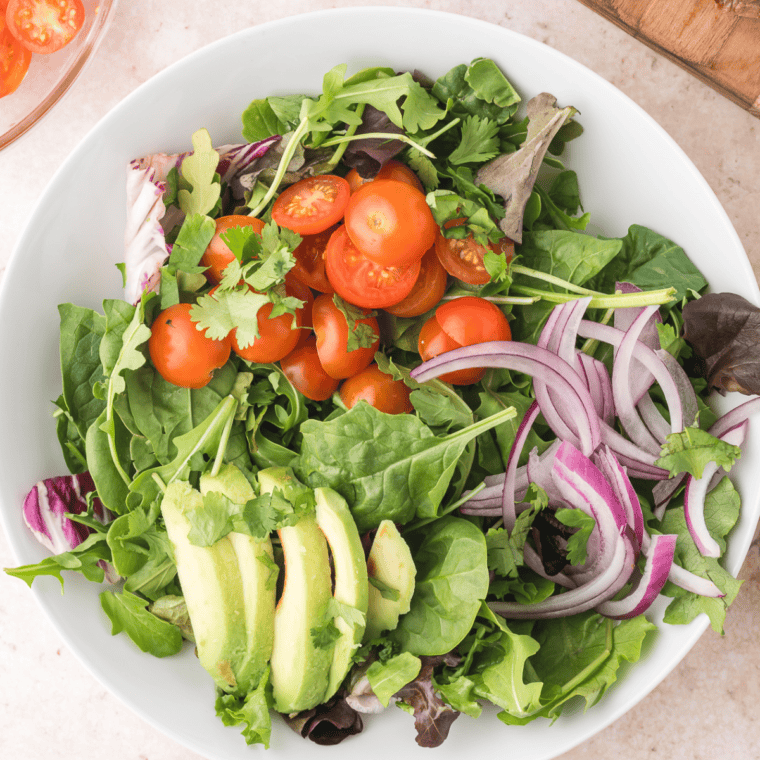 Combining salad ingredients with carne asada, tossing with dressing, and garnishing with queso fresco and lime.