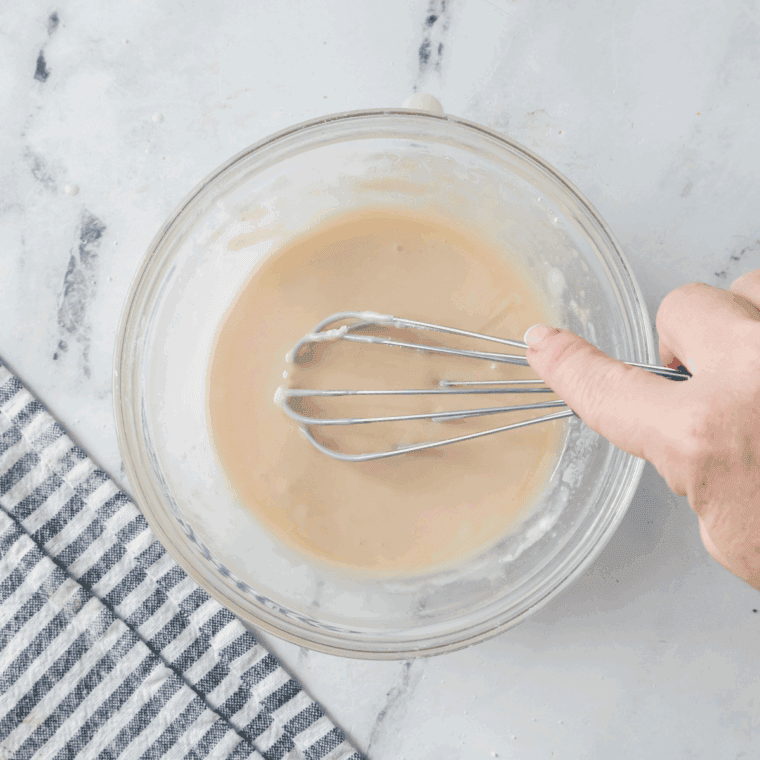 Whisking maple glaze in a bowl until thick and pourable