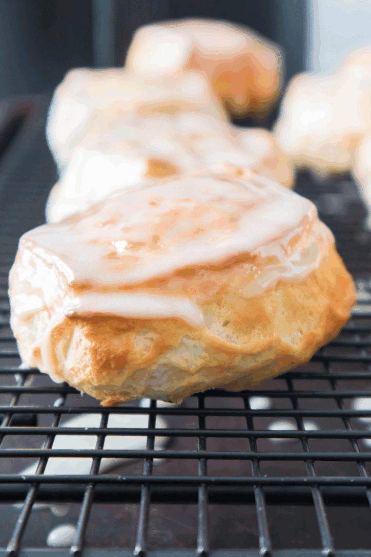 Two maple bar donuts on parchment with glaze dripping down the sides