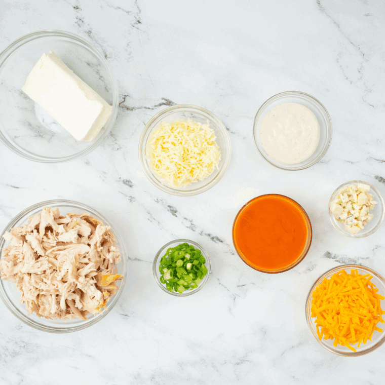 Ingredients for Hooters Buffalo Chicken Dip including shredded chicken, cream cheese, ranch, wing sauce, and cheddar on a kitchen counter
