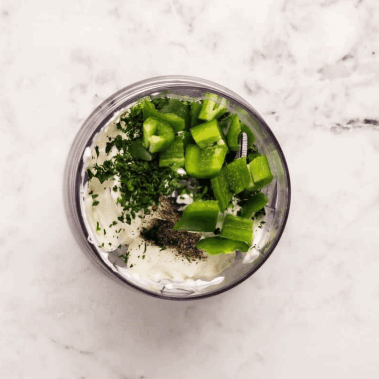 Fresh avocado, sour cream, lime juice, and spices in a blender ready to be mixed.