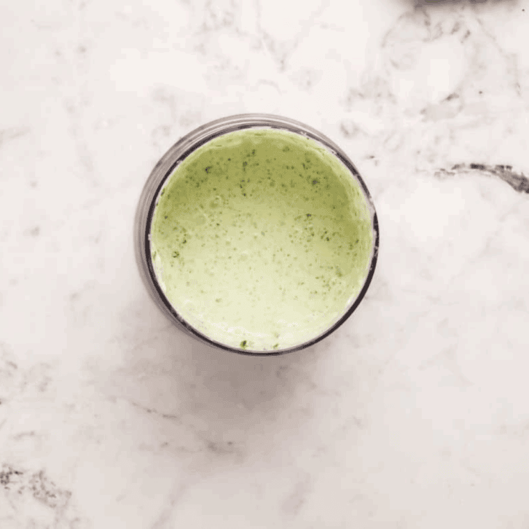 Creamy avocado lime sauce being blended until smooth in a food processor.