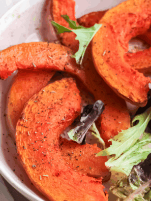 Golden brown air fryer pumpkin wedges served on a plate with herbs and dipping sauce.