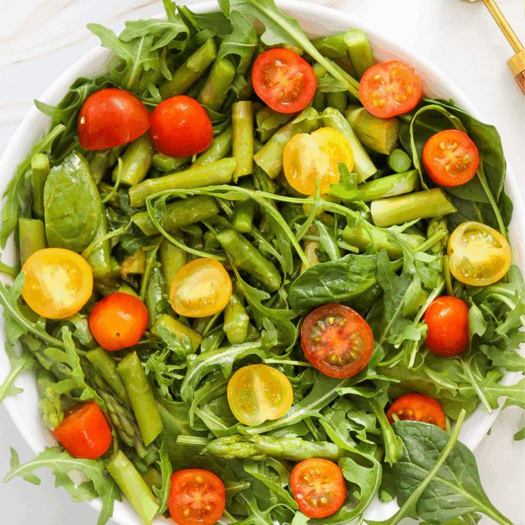 Finished asparagus spinach salad tossed with dressing and topped with goat cheese and fresh herbs.