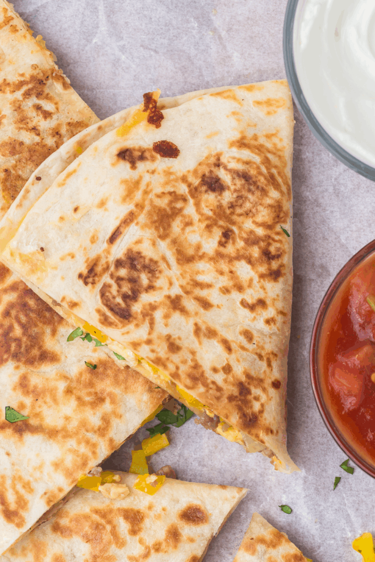 Golden breakfast quesadillas cooking on a Blackstone griddle, stuffed with scrambled eggs, sausage, and cheese