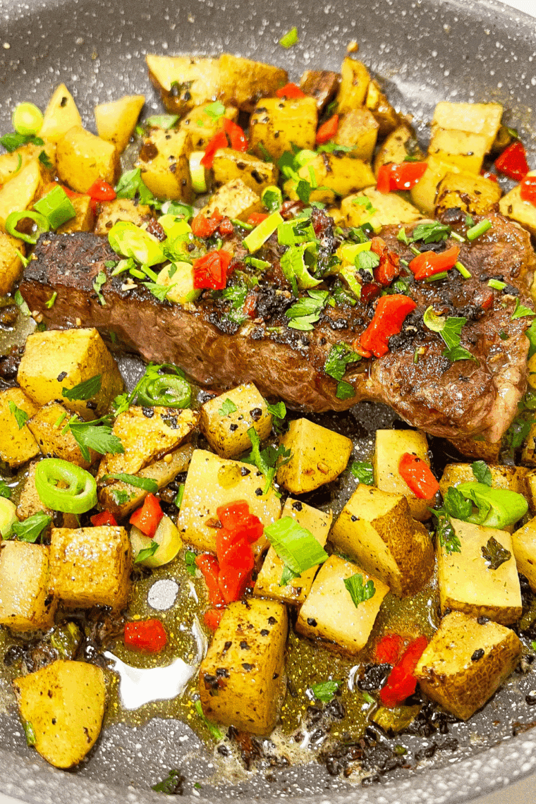 Skillet filled with juicy sliced steak and golden potatoes topped with cowboy butter and fresh herbs.


