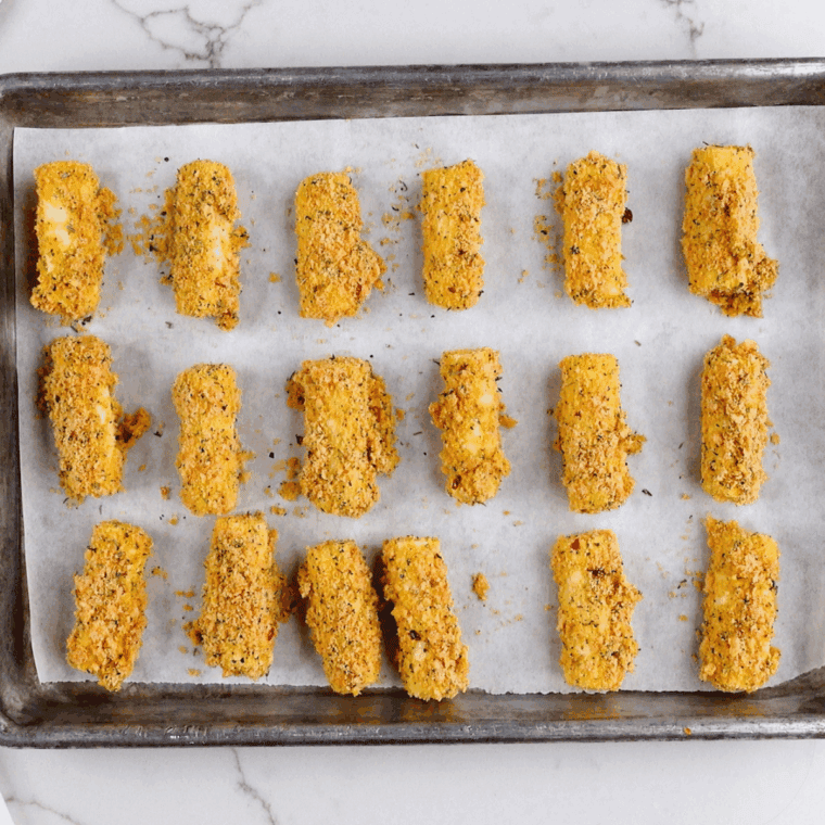 
Breaded mozzarella sticks arranged on a parchment-lined tray ready to freeze.
