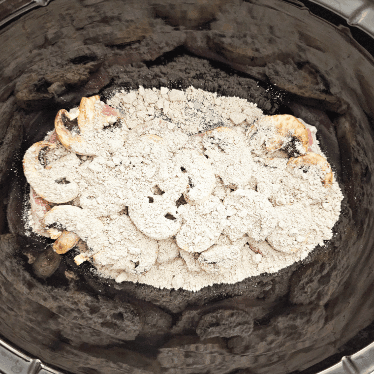 Brown gravy mix sprinkled over mushrooms with water poured in.
