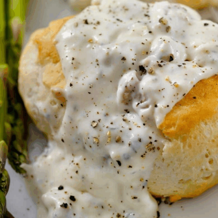 Creamy homemade Hardee’s-style sausage gravy served over flaky biscuits on a white plate.

