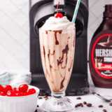 Glass of homemade Ninja Creami McDonald’s chocolate milkshake topped with whipped cream and a cherry.