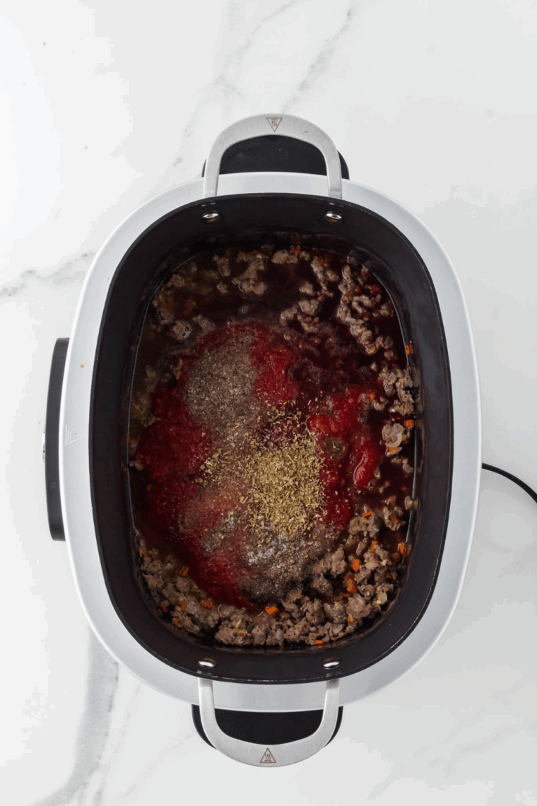 Stirring in tomato paste, crushed tomatoes, broth, and seasonings into the browned meat and vegetables.