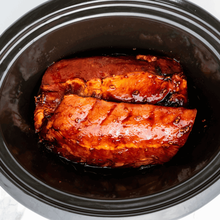 Raw ribs in a slow cooker being brushed with BBQ sauce over Dr Pepper