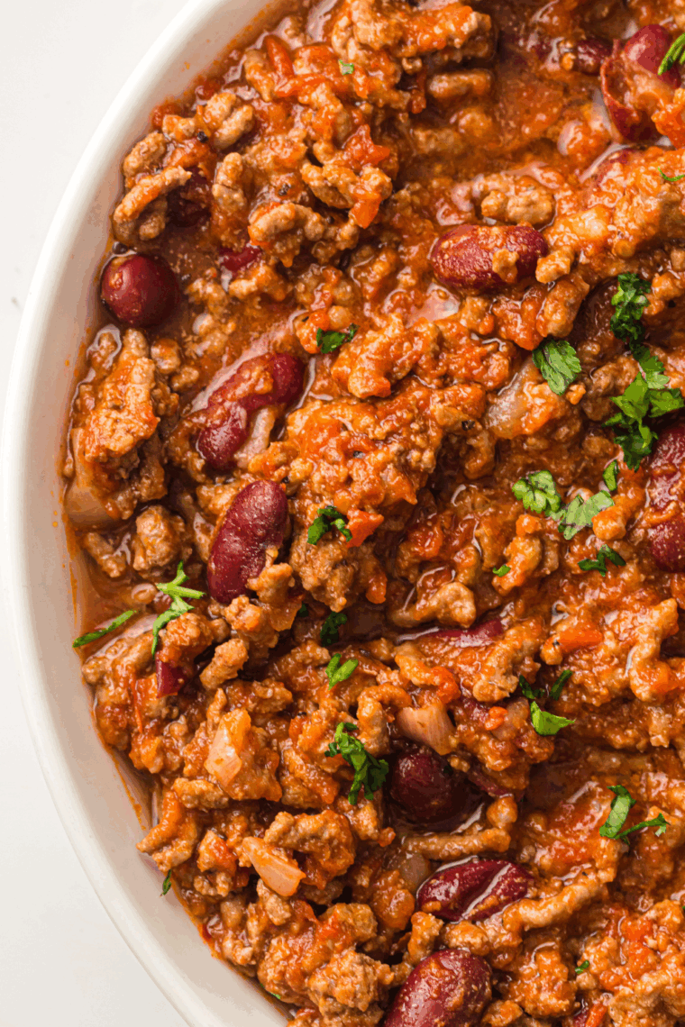 Hearty bowl of Texas Roadhouse-style chili topped with shredded cheese and fresh onions.