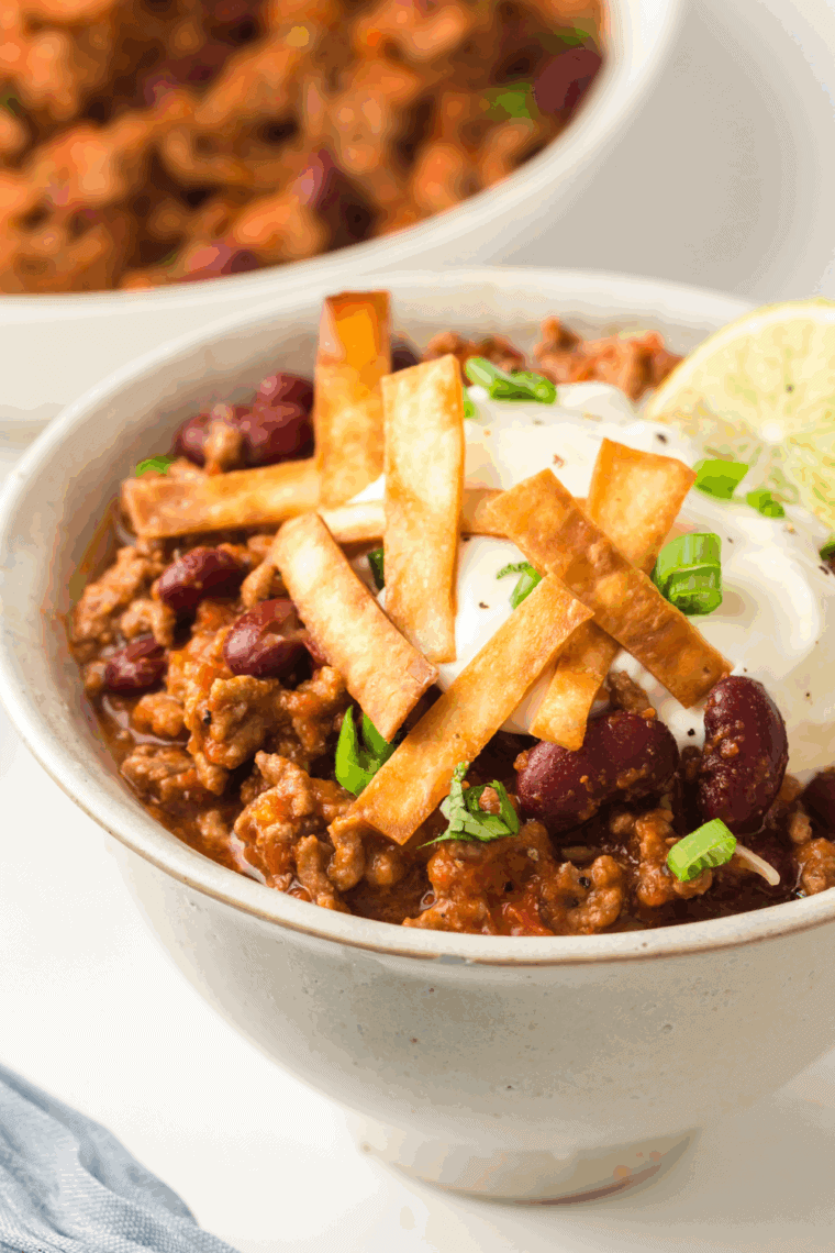Hearty bowl of Texas Roadhouse chili topped with shredded cheese, sour cream, and chopped onions.