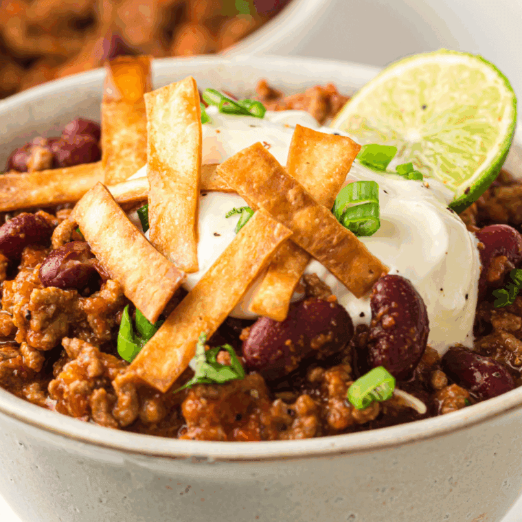 Bowl of Texas Roadhouse-style chili with ground beef, topped with shredded cheese and chopped onions.