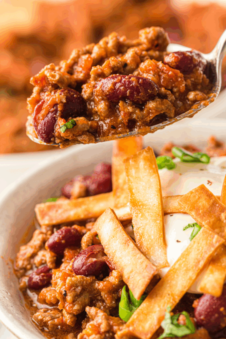 Bowl of homemade Texas Roadhouse chili topped with cheese, sour cream, and chopped onions.