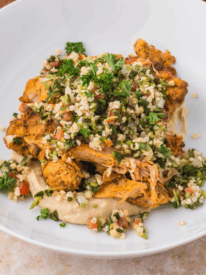 Bowl filled with Trader Joe’s Shawarma Chicken, hummus, and cauliflower tabbouleh, served with fresh vegetables.