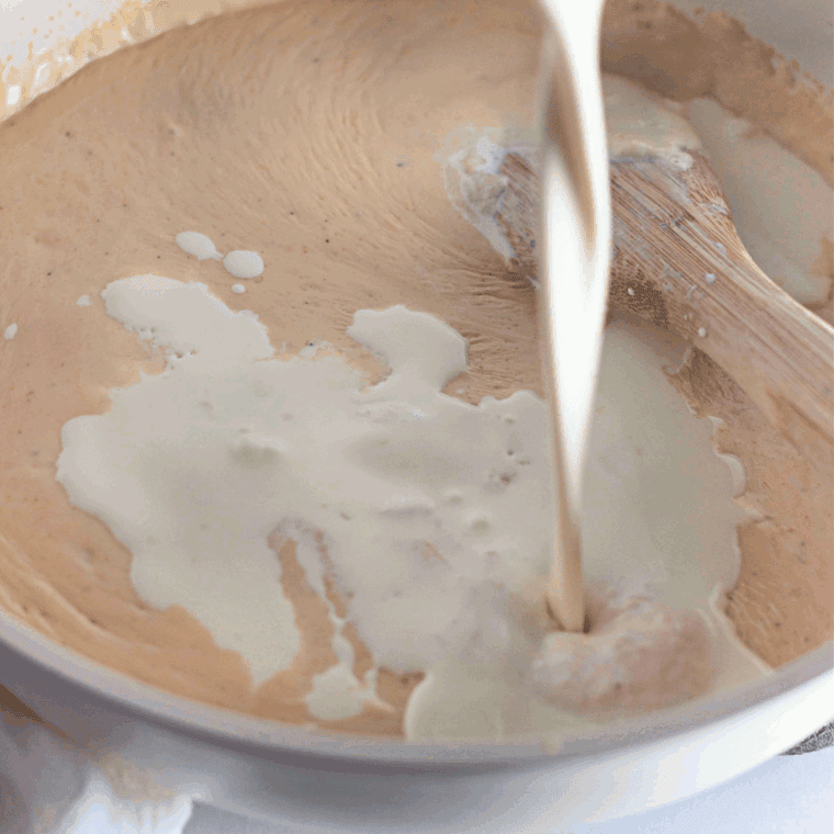 Whisking milk into roux until thickened, then melting shredded cheddar and spices into a smooth, creamy cheese sauce.