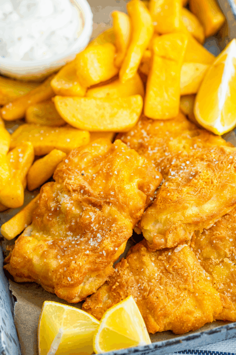 Plate of golden, crispy Arthur Treacher’s style fish and chips with lemon wedges and tartar sauce.