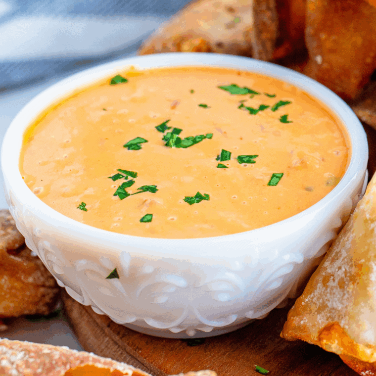 Small bowl of dipping sauce next to blistered shishito peppers on a plate