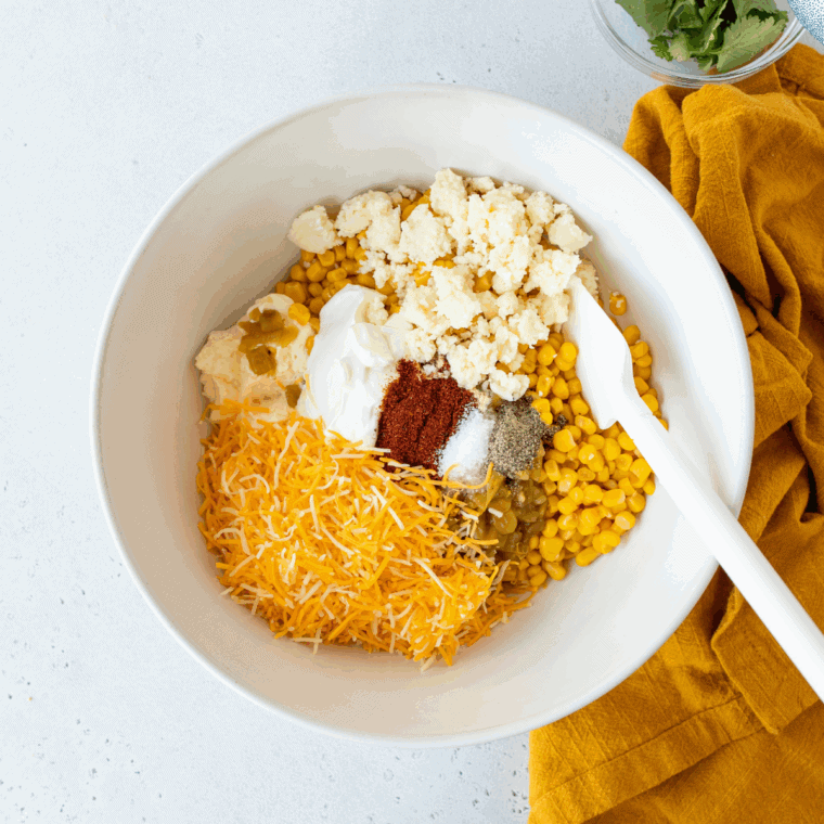 Corn, mayo, sour cream, and spices stirred together in a glass bowl for an elote bake