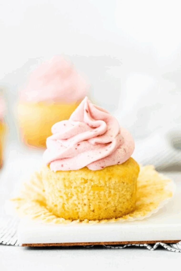 Homemade lemon raspberry cupcakes topped with creamy frosting and garnished with fresh raspberries and lemon zest.