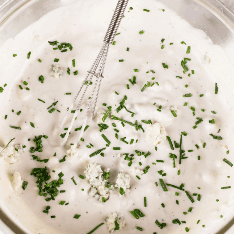 Homemade Ina Garten buttermilk blue cheese dressing in a glass jar, garnished with chives.