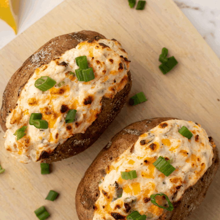 Shrimp stuffed baked potato topped with melted cheese and fresh herbs on a white plate.
