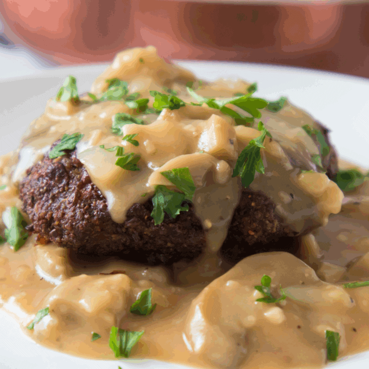 Plate of juicy chopped steak covered in mushroom & onion gravy