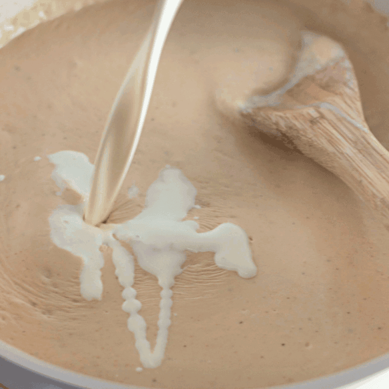 Milk being whisked into a saucepan to create a smooth, creamy sauce base.