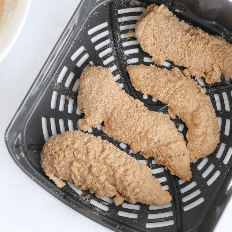 Coated chicken tenders arranged in an air fryer basket, golden brown and ready to serve with dipping sauces.