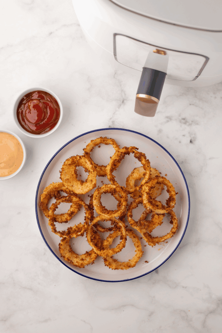 Golden, crispy Dairy Queen-style onion rings stacked on a plate with dipping sauce