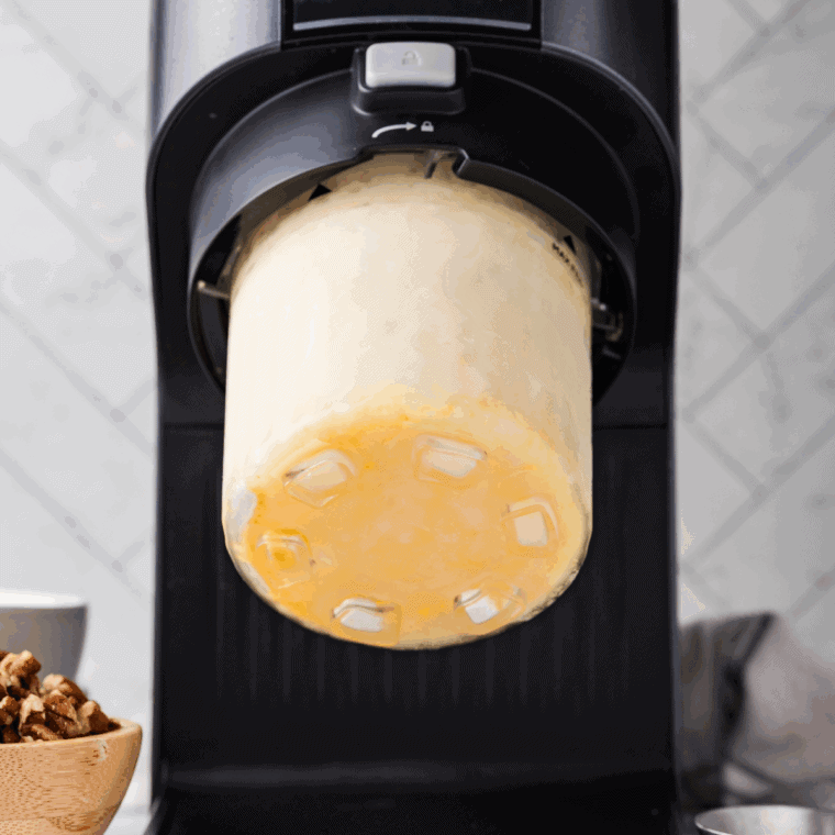 Frozen pumpkin base inside the Ninja Creami processing on the ice cream setting.