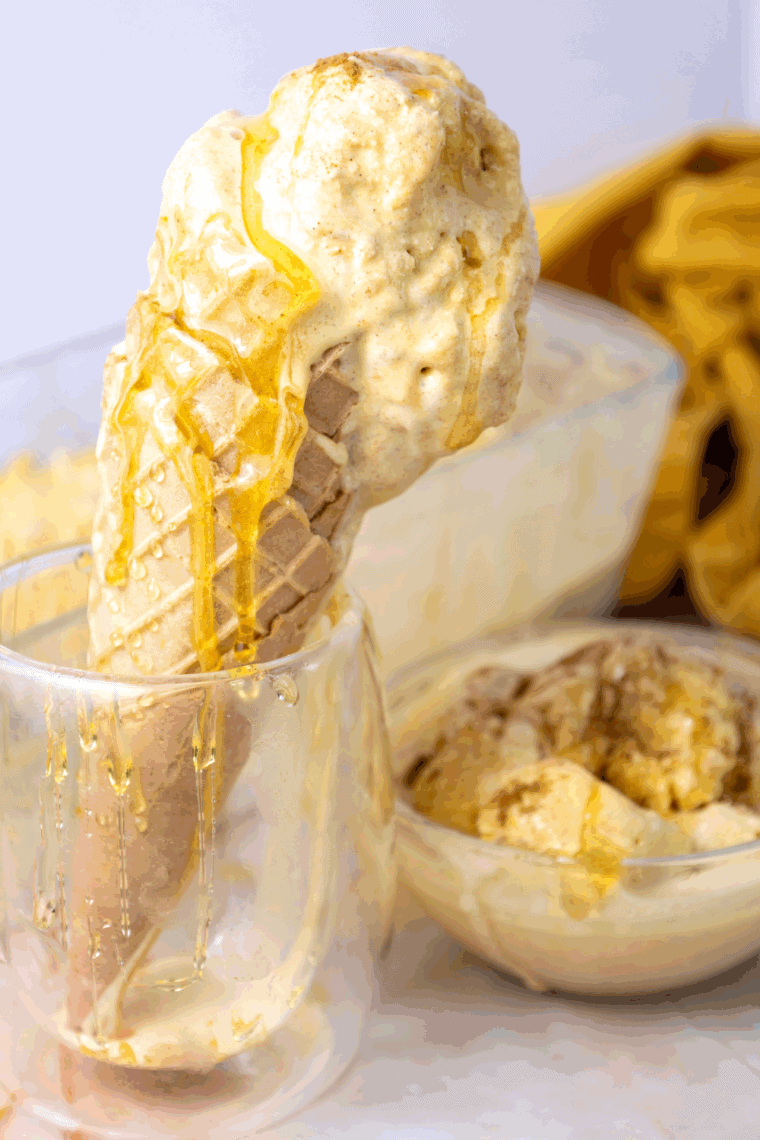 Bowl of homemade Ninja Creami pumpkin cheesecake ice cream topped with whipped cream and graham cracker crumbs.